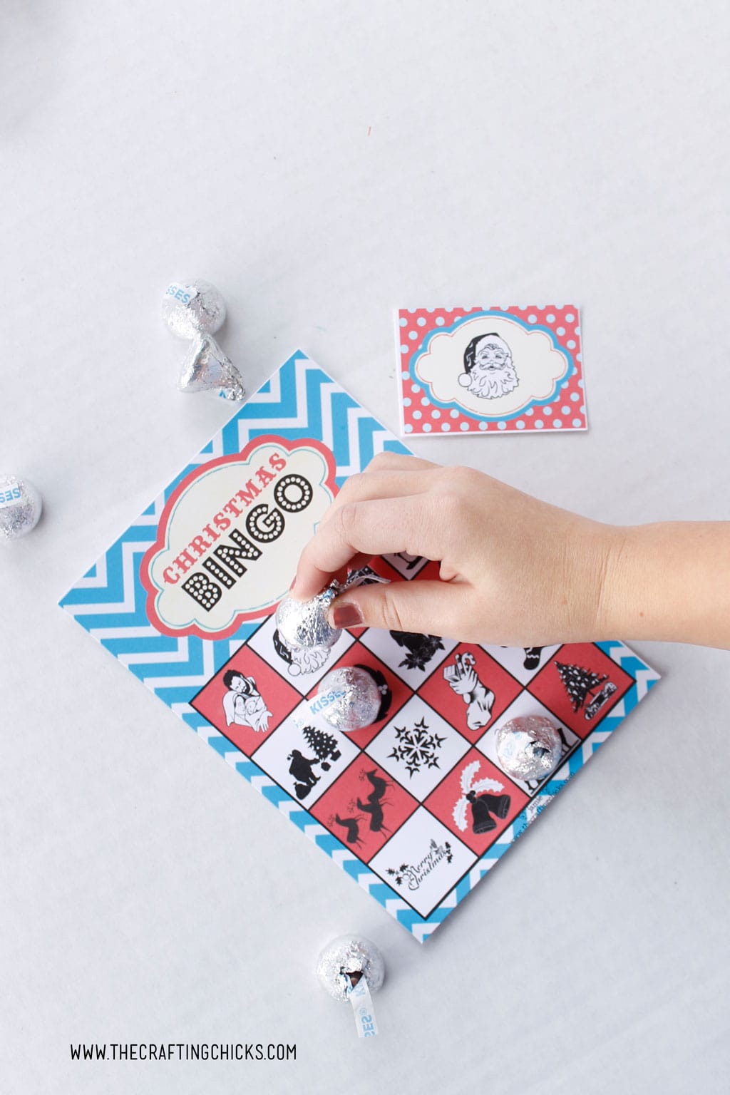 Free Printable Christmas Bingo Game with child's hand playing the game with Hershey Kisses.