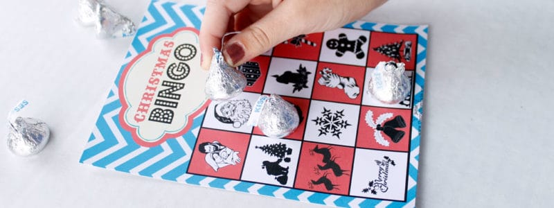 Free Printable Christmas Bingo Game with child's hand playing the game with Hershey Kisses.