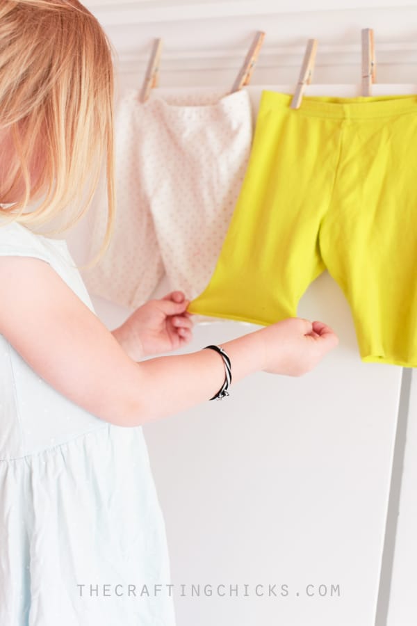 Little girl pulling the bottom hem on the no-sew shorts that have been cut from leggings.