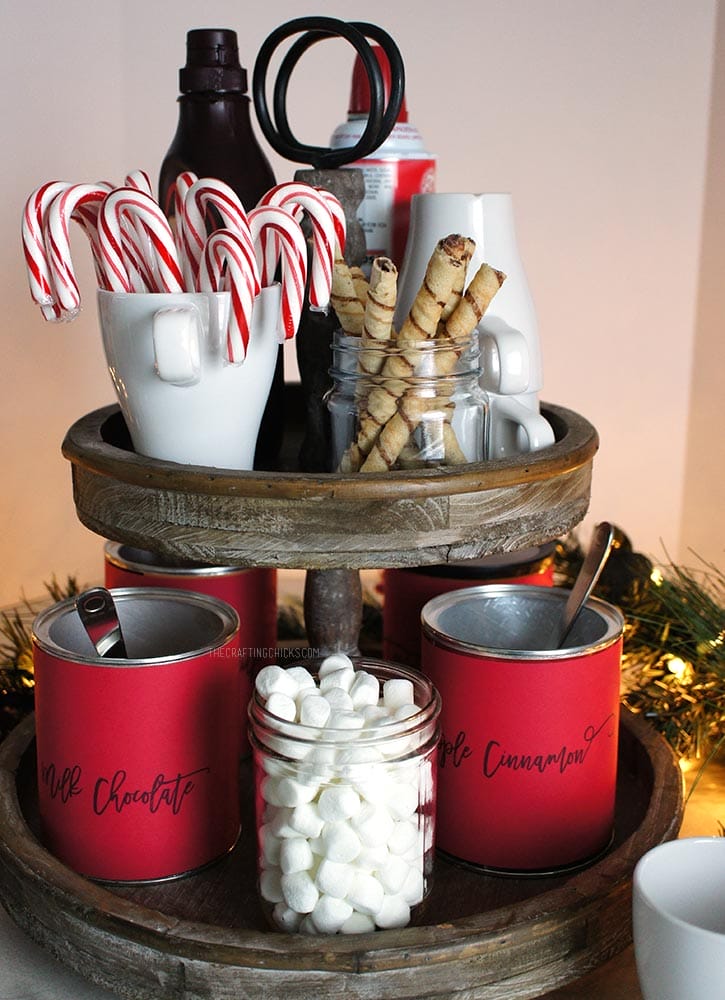 Rustic 2-tiered stand with hot chocolate mix, candy canes, marshmallow, mugs and whipped cream to make a Hot Chocolate Station.