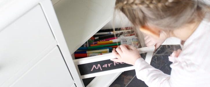 Little girl reading into a box full of markers