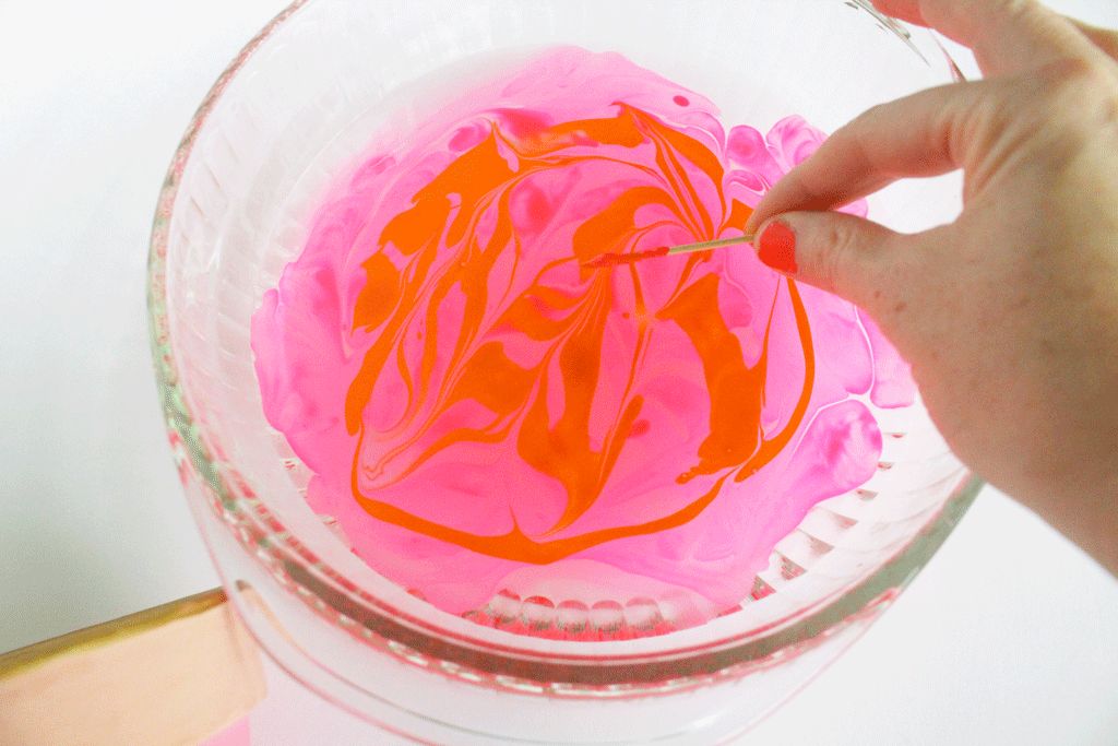 Swirling nail polish colors in a glass dish with water using a toothpick.