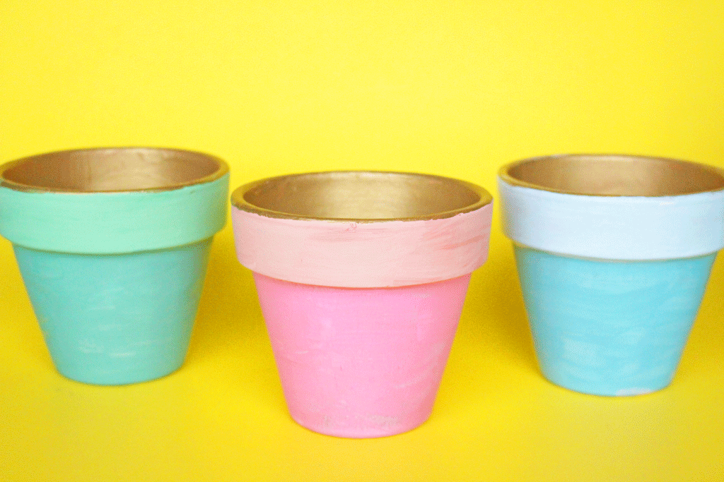 A green, pink, and blue planter painted sitting on a yellow backdrop