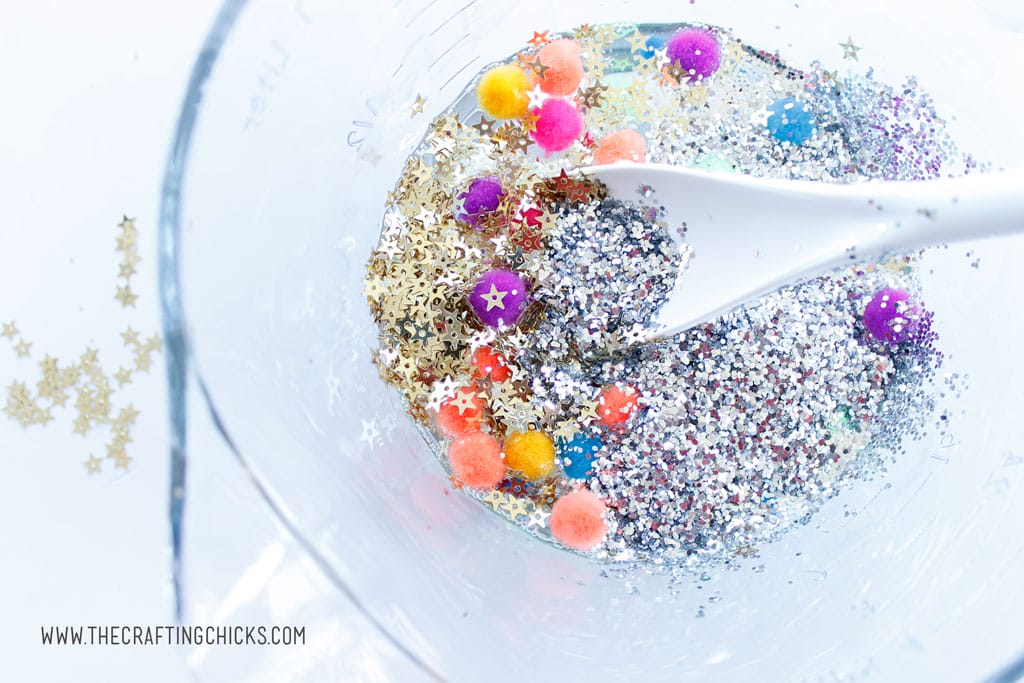 Adding glitter and pom poms to galaxy slime.
