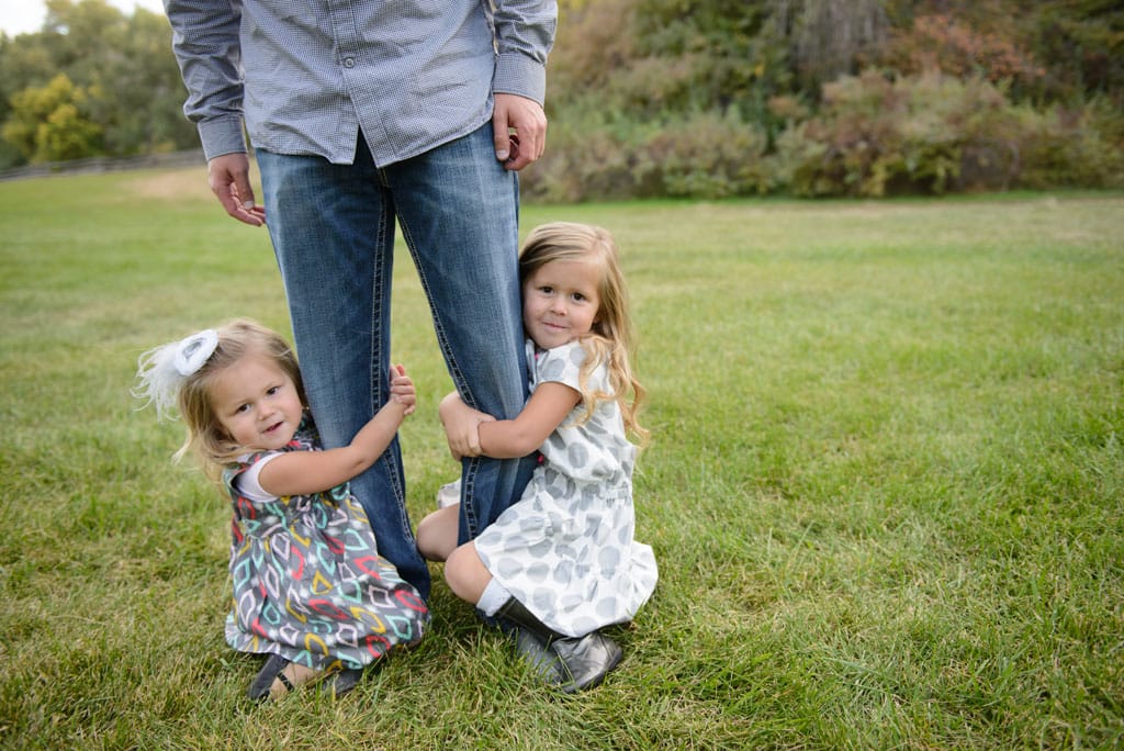 2 little girls holding on to dad's leg