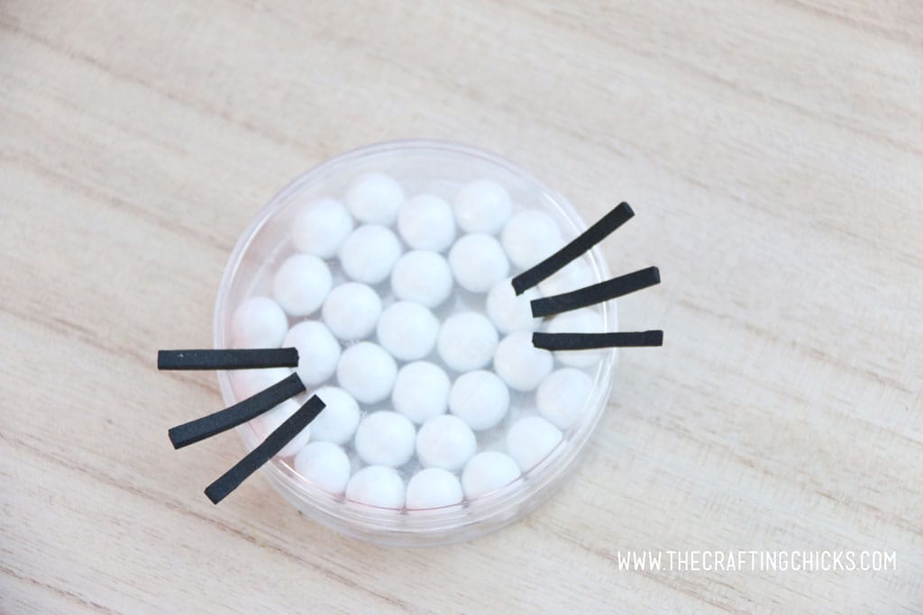 Black foam whiskers added to a clear round favor container filled with white Sixlets to make a Hello Kitty Face