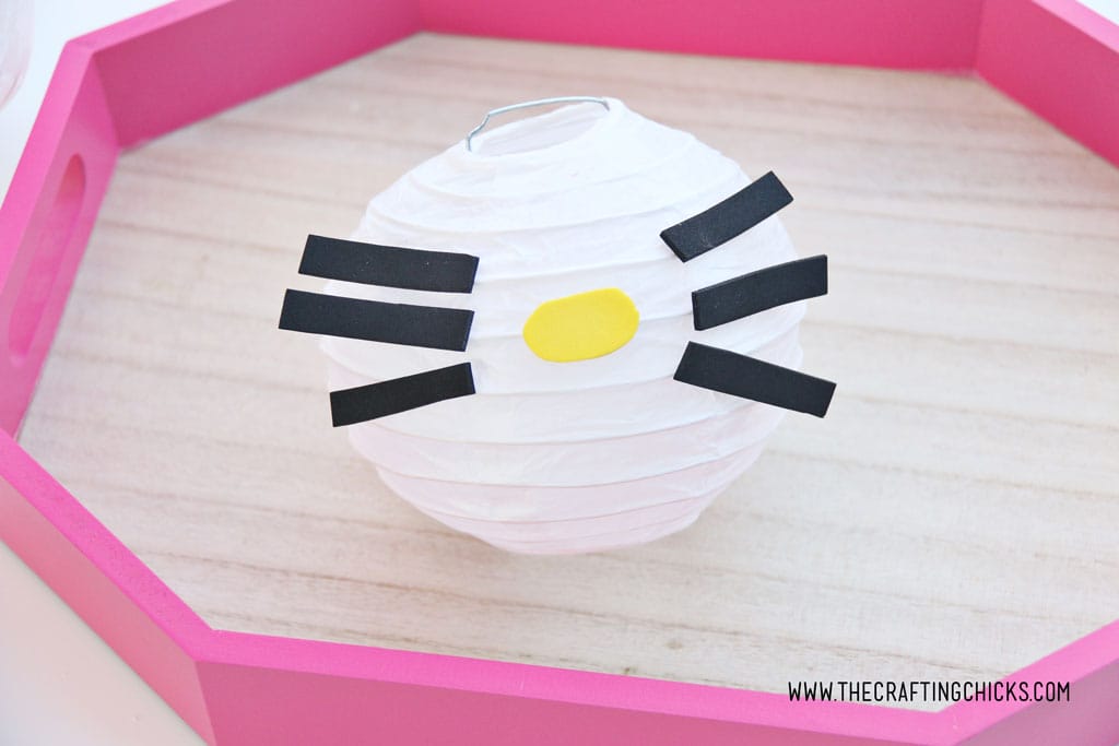 Yellow foam nose added to white mini paper lantern with cut out foam shapes to make Hello Kitty DIY Paper Lanterns
