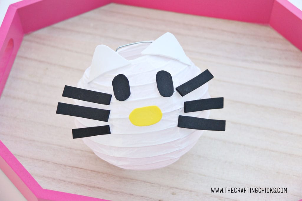White foam kitty ears added to White mini paper lantern with cut out foam shapes to make Hello Kitty DIY Paper Lanterns