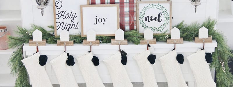 White fireplace and mantel decorated with white knit stockings and Christmas prints in frames.