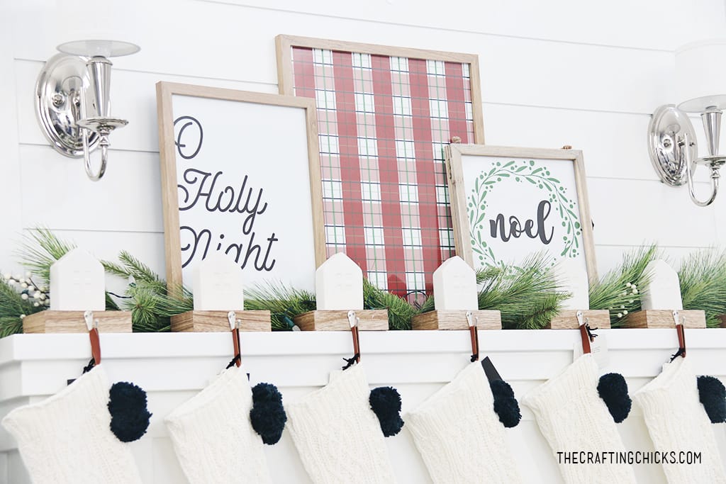 Noel Wreath print framed on a white mantel next to a red plaid background print and Oh Holy Night print.