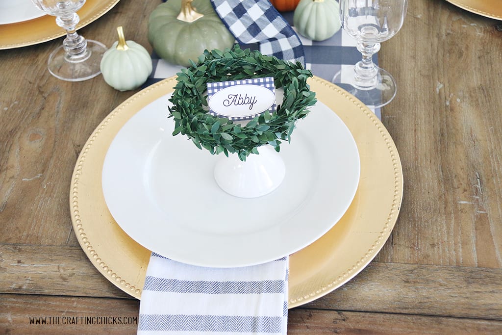 Thanksgiving navy and white check, printable place cards. Styled on a gold charger and white plate and decorated with a green wreath.