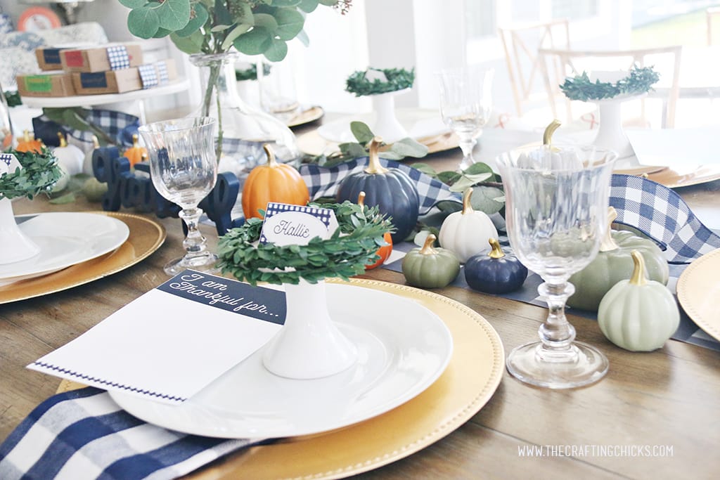 Thanksgiving table styled with navy and white check print and mini pumpkins and gold chargers.