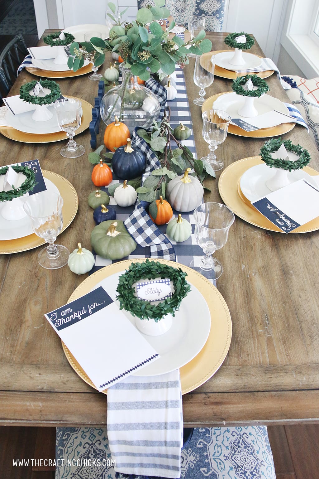 Thanksgiving table set with gold chargers and white plates. Printable navy and white placecards with wreaths and mini pumpkins.