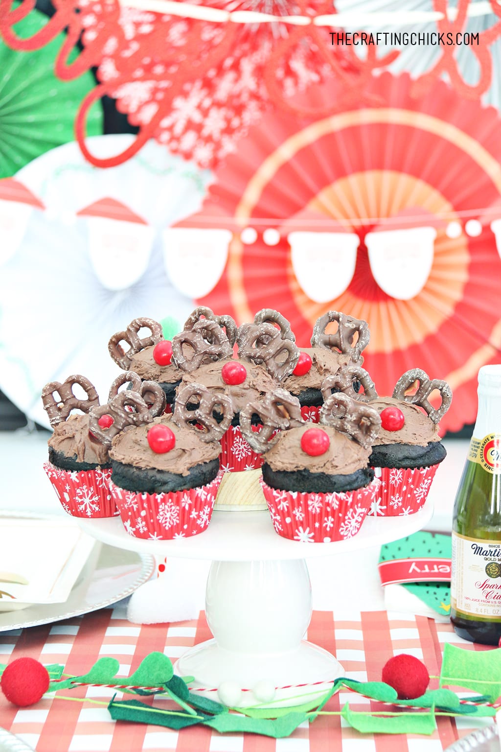 Reindeer cupcakes on decorated party table with red and green paper fan background.