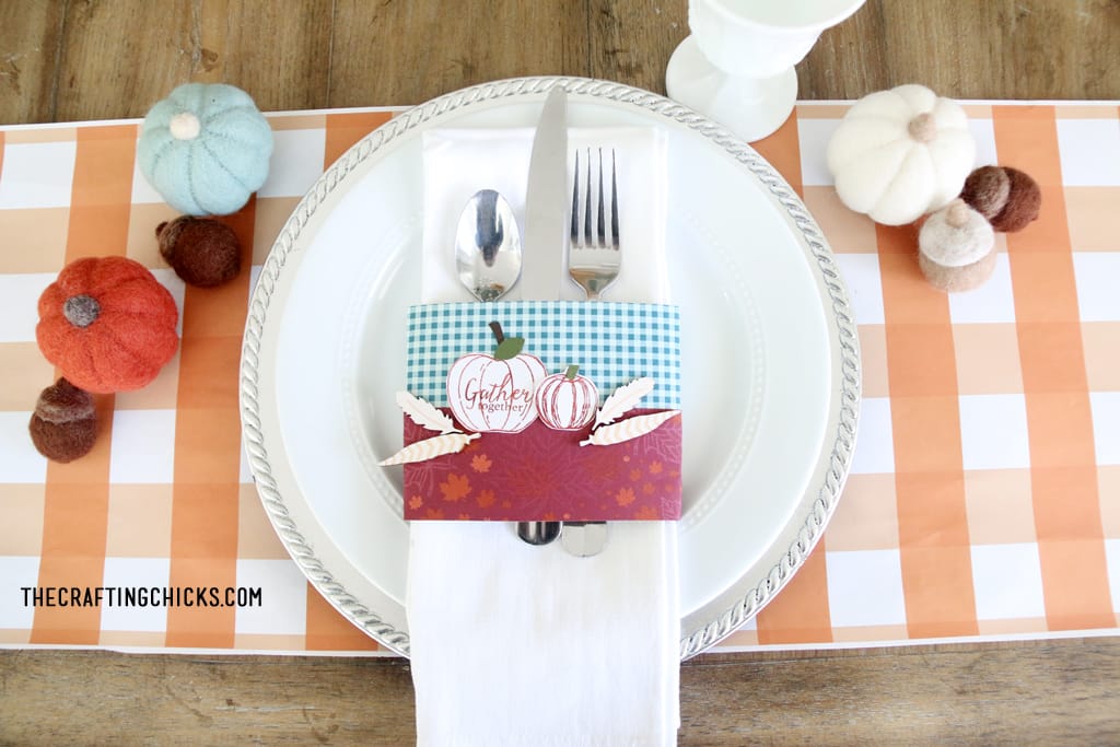 Thanksgiving place setting with orange plaid place mat, white plate, and stamped napkin ring with pumpkins.