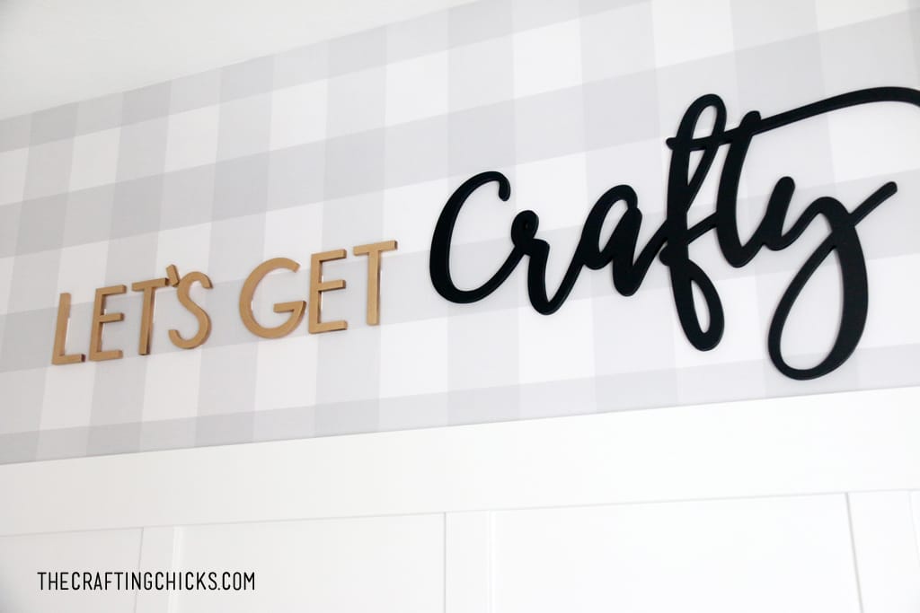Gray plaid wallpaper on a wall with gold and black cut out letters spelling Let's Get Crafty.