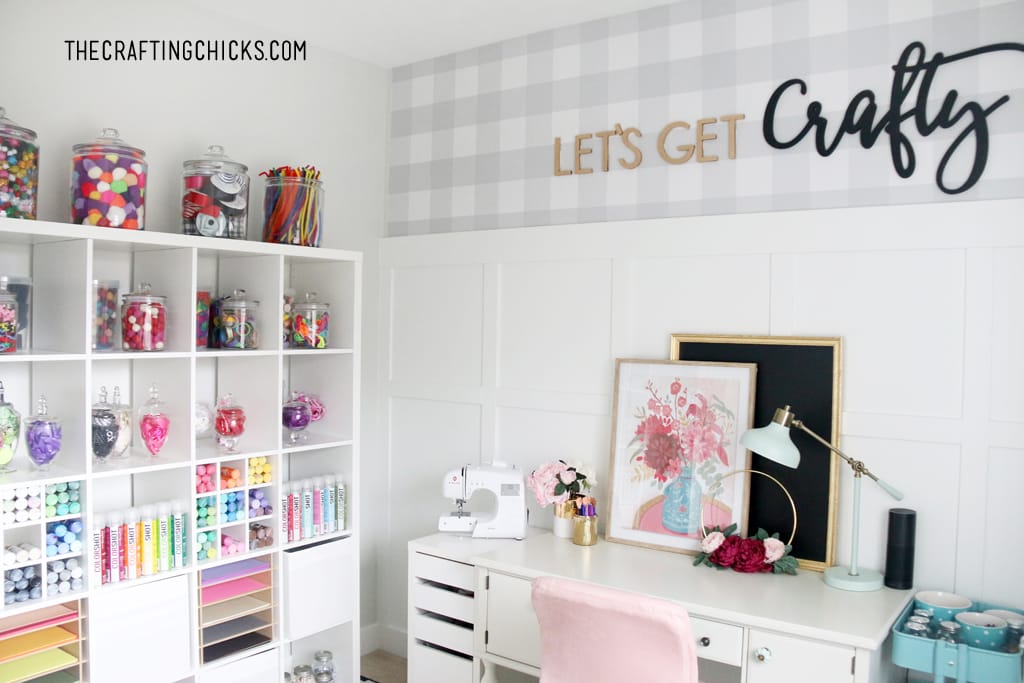 Craft room with white shelves decorated with colorful jars full of craft supplies. White desk with pink plush office chair.