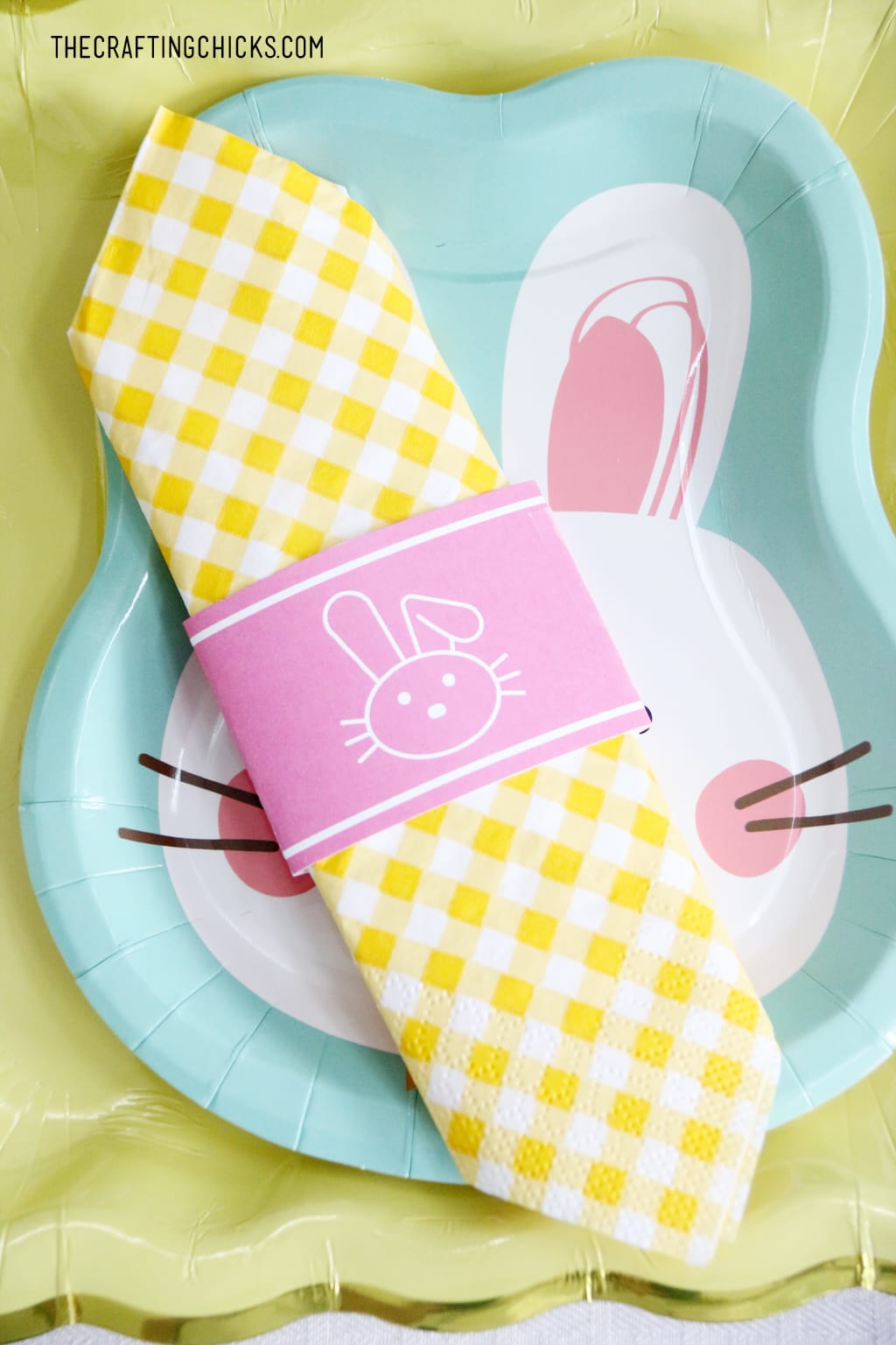 Easter table for kids with bunny paper plates, yellow gingham napkin and bunny decorations. Big Pink bunny printable backdrop