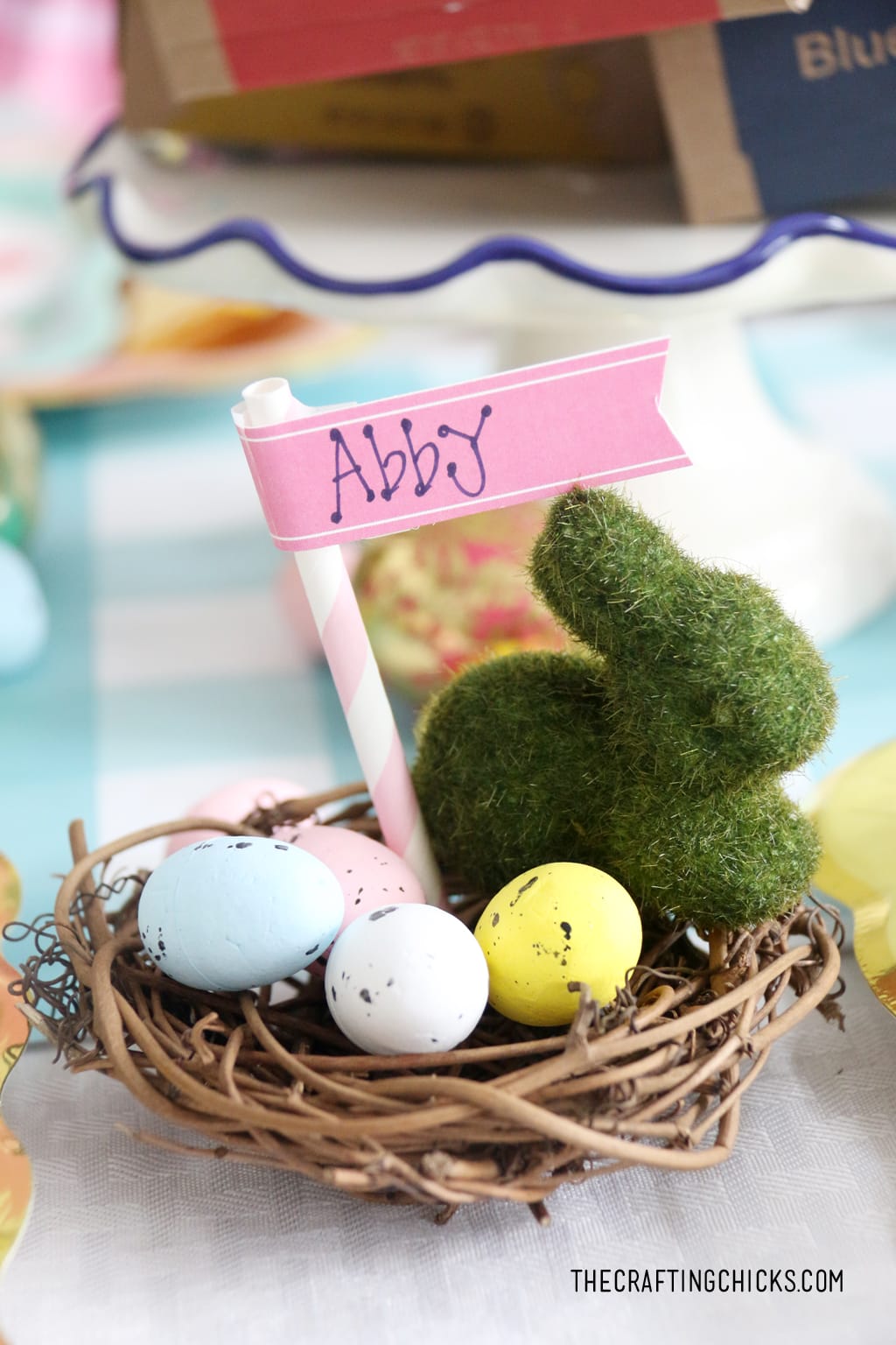 Easter table for kids with faux grass bunny decoration and faux eggs as in a nest with a name tag as table decoration.