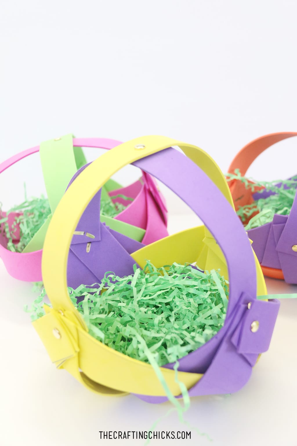 Foam strips woven together to make a basket with brads, filled with green Easter grass.