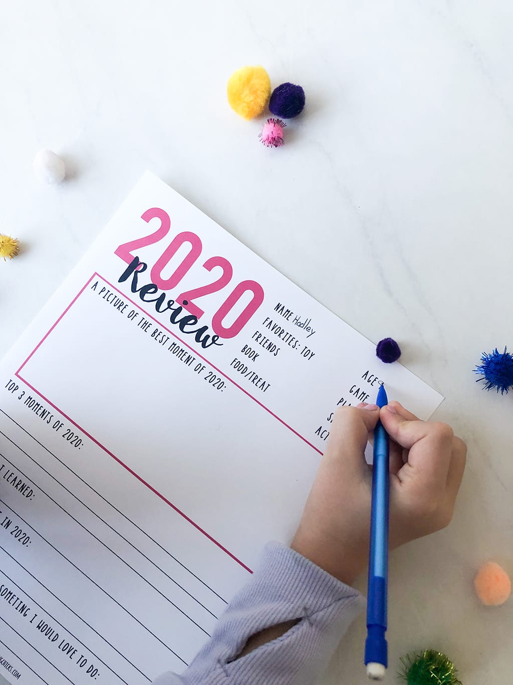 Little girl using a pencil to fill in a 2020 Year in Review printable with pink type.