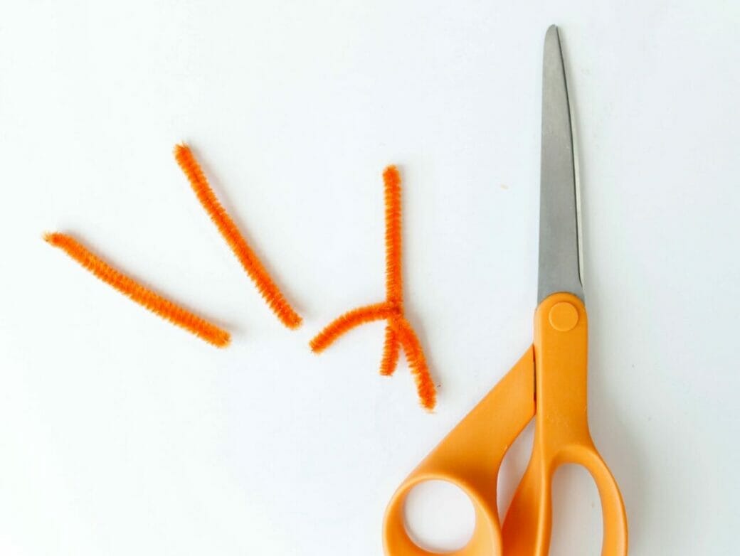 Orange pipe cleaners on a white background with scissors.