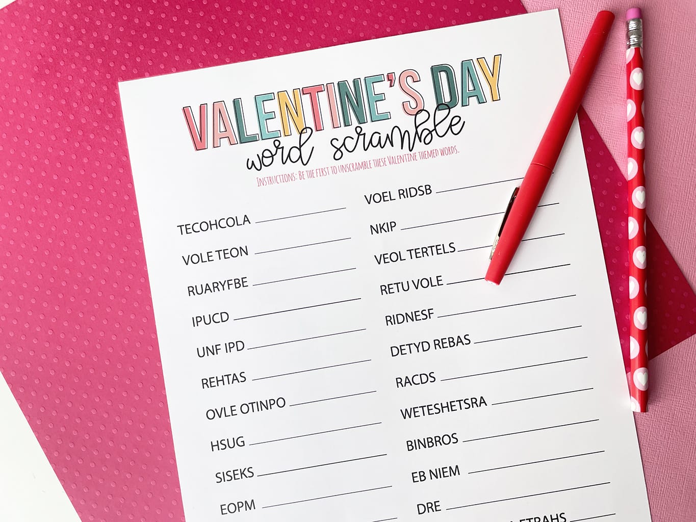 Valentines Day Word Scramble Printable Game printed out and placed on a dark pink and light pink paper backdrop. With a red fineline marker and a Valentine pencil.