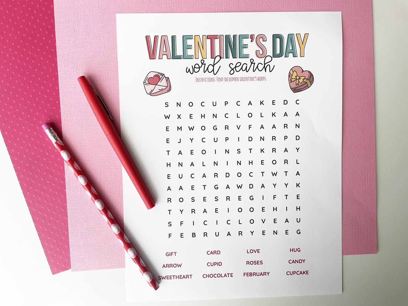 Valentine's Day Word Search Printable, printed out and placed on a light pink paper and a dark pink paper background. Valentine pencil and red fine line marker on the side.